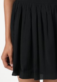 Jupe plissée noire en tissu léger et texturé. Présente une taille et un ourlet évasé pour une silhouette en A.