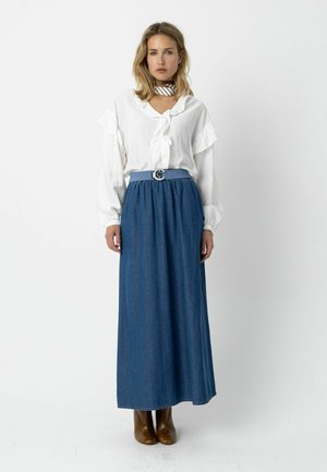 Biela blúzka s volánikovými rukávmi, kombinovaná s modrou džínsovou maxi sukňou. Oblečenie dopĺňa svetlomodrý opasok so striebornou prackou a hnedé členkové čižmy.