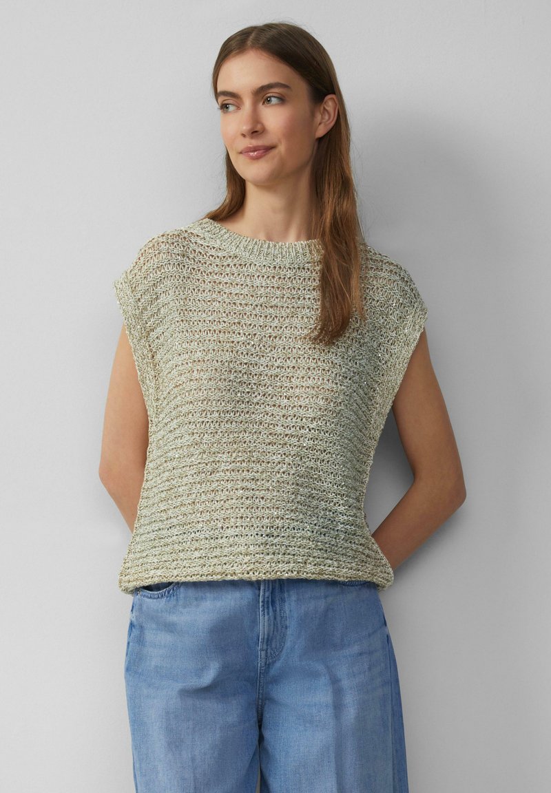 Jasnozielony dzianinowy top z krótkim rękawem, luźny krój, z teksturowanym wzorem, w zestawie z luźnymi niebieskimi dżinsami.