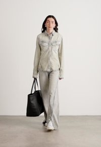 Giacca in denim con due tasche sul petto e maniche lunghe, abbinata a jeans a campana coordinati. Borsa tote nera. Design minimalista, colore grigio chiaro.