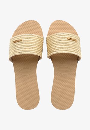 Sandales beiges à enfiler avec semelles texturées et brides en tissu tissé, portant le nom de la marque embossé sur les semelles intérieures et de petits logos métalliques sur les brides.