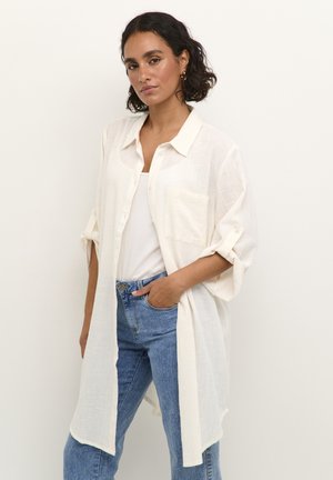 Chemise blanche légère à boutons, avec une poche avant, des manches retroussées et une coupe décontractée, associée à un jean taille haute bleu.