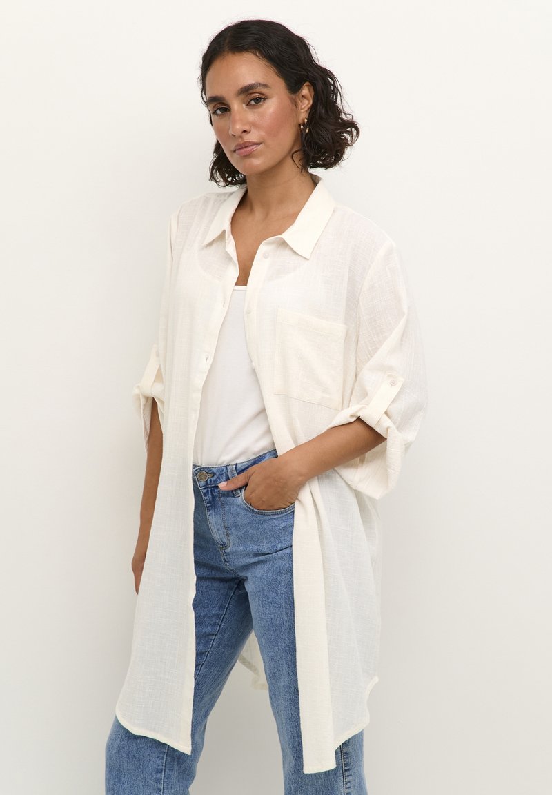 Chemise blanche légère à boutons, avec une poche avant, des manches retroussées et une coupe décontractée, associée à un jean taille haute bleu.