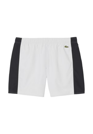 White swim shorts with black side panels, elastic waistband, and Lacoste crocodile logo on the left front. Smooth, lightweight fabric.