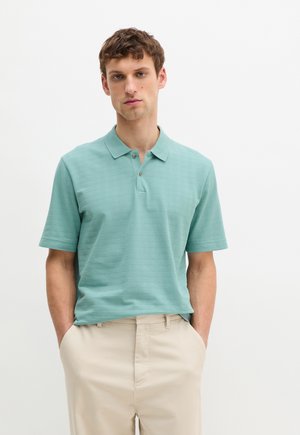 Polo shirt in light teal with a textured pattern, short sleeves, and a two-button collar, paired with beige pants.