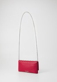 Sac en cuir rouge à bandoulière avec chaîne en argent, forme rectangulaire plate, ornements à clous le long du haut, portant la marque "Steve Madden" à l'avant.