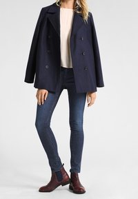 Giacca blu navy doppiopetto, abbinata a jeans a righe verticali. Stivaletti marroni alla caviglia con pannelli elastici laterali. Simple top crema sottostante.