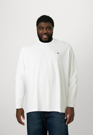 Witte langesleeve t-shirt van katoen, met een ronde hals en een klein groen logo op de borst, gecombineerd met donkerblauwe jeans.