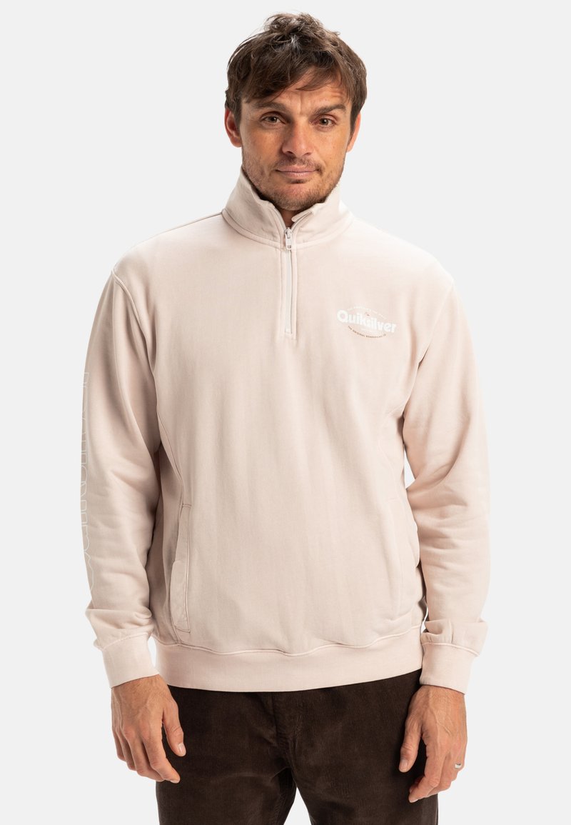 Light pink quarter-zip pullover made of soft fabric, featuring a logo on the chest and text down the sleeve, with ribbed cuffs and hem.