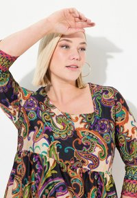 Kleurrijke jurk met patronen, met 3/4 mouwen, vierkante halslijn en een uitlopende silhoette, met paisley ontwerpen in groen, oranje, paars en zwart.