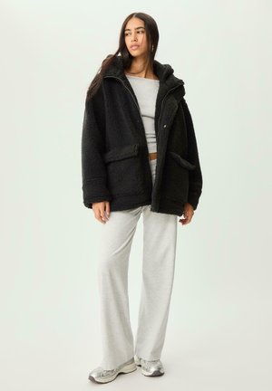 Zwarte fleecejack met een capuchon, twee voorkruimelzakken en een rits, gecombineerd met lichtgrijze wijde sweatpants en zilveren sneakers.