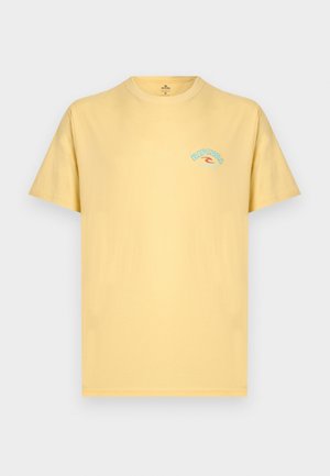 Svetlo rumena majica s kratkimi rokavi in majhnim modro-rdečim logotipom "Rip Curl" na zgornjem levem delu prsnega koša, enobarvna podlaga.