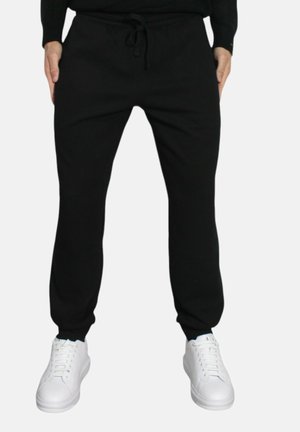 Pantaloni sportivi neri con vita elasticizzata, cordino e polsini aderenti, abbinati a sneakers bianche. Tessuto morbido, design semplice.