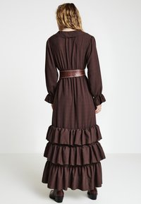 Braunes langärmliges Maxikleid mit gerafftem Saum, Kragen und braunem Gürtel mit Nietenakzenten an der Taille.