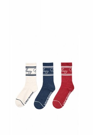 Trois chaussettes montantes côtelées en blanc, marine et rouge, chacune avec des rayures contrastées et un texte en cursive près du haut et du bas.