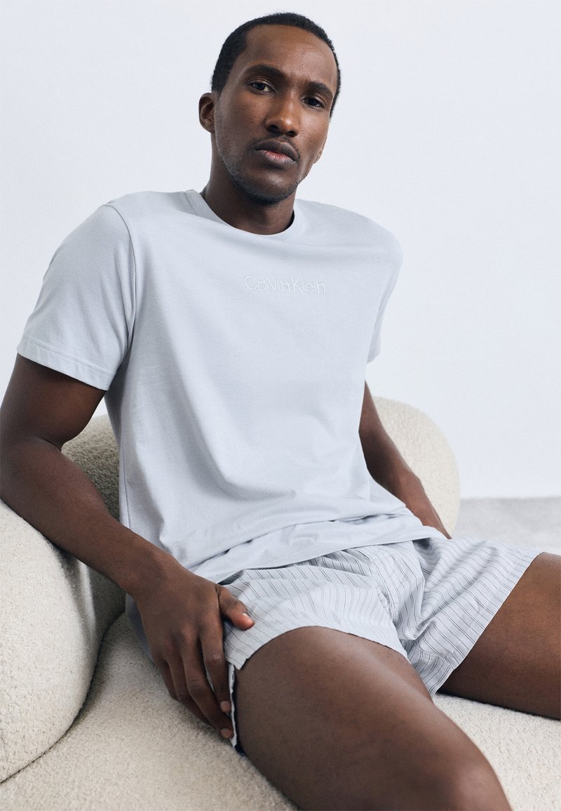 Világosszürke pamutt-shirt, diszkrét "Calvin Klein" hímzéssel, csíkos szürke sorttal párosítva. Sima tapintású, laza szabású.