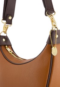 Braune Lederhandtasche mit glatter Textur, ausgestattet mit einem dunkelbraunen Riemen, goldfarbener Hardware und einem kleinen Logoanhänger, der an einer Kette befestigt ist.