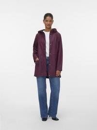 Vattentålig burgundy-jacka med huva, fäst med tryckknappar, och två sidofickor, bärs över en vit topp och blå jeans.