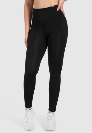 Zwarte leggings met een hoge tailleband, rekbare stof en zijzakken. Draag met witte sportieve schoenen.