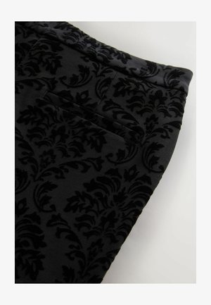 Black fabric with raised velvet floral damask pattern and a welt pocket, shown on a light background.
