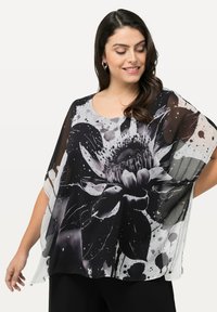 Doorzichtige zwart-witte top met een bloemenpatroon, gekenmerkt door grote zwart-grijze bloemen, kleurspatters en een ronde halslijn.