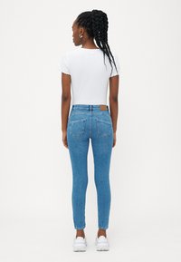 Vaqueros ajustados de color azul con una cintura media, diseño de cinco bolsillos y costuras en contraste. Combinados con una blusa de canalé blanca y zapatillas blancas.