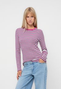 Långärmad skjorta med horisontella ränder i rosa och vitt, med en rosa rund halsringning och en slim fit. I kombination med ljusblå jeans.