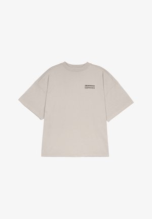 Lühikeste varrukatega, ülemõõduline t-särk heleses beezis puuvillas, mis sisaldab väikest musta graafilist trükist rinnal. Ümar kaelus, sirge äär.