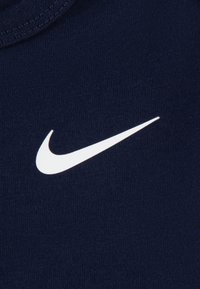 Tricou bleumarin din bumbac, cu un logo Nike Swoosh alb proeminent în zona pieptului stâng. Textură netedă și guler rotund.