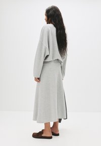 Svetlo sivá, oversized mikina a zodpovedajúca sukňa po členky z mäkkej látky. Sukňa má jemný tvar do A a postranné rozparky.