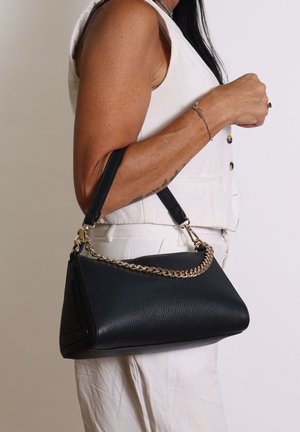 Borsa in pelle nera con texture, decorata con una catena dorata e due manici. La borsa ha una forma triangolare ed è tenuta da una persona.