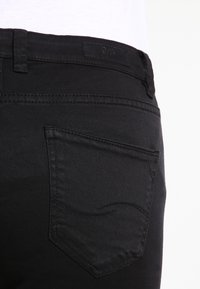 Vaqueros de mezclilla negra con un bolsillo trasero distintivo con costuras curvas, una textura suave y una etiqueta resistente en la cintura.