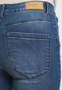 Dark blue denim jeans with a smooth texture. Features back pockets and a rectangular leather tag marked "VERO MODA DENIM." Classic five-pocket design.