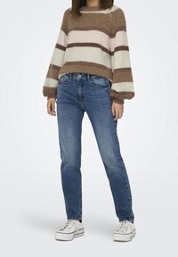 Brązowy i beżowy sweter dzianinowy w paski z balonowymi rękawami, zestawiony z niebieskimi dżinsami prostymi i białymi trampkami. Gładka tekstura i luźny krój.
