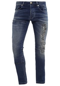 Jeans in denim blu scuro con toppe strappate e sbiadite, design a cinque tasche, chiusura con bottone e zip in vita.