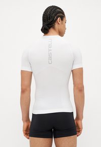 White short-sleeved athletic shirt with fitted design and mesh texture, featuring a logo on the back. Worn with black shorts.