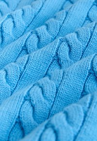 Svetlomodrý pletený materiál s textúrovaným káblovým vzorom, ktorý obsahuje prepletené vlákná vytvárajúce trojrozmerný efekt.