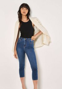 Top sin mangas negro de canalé, jeans azules de tiro alto, y una chaqueta ligera a rayas. Los jeans tienen un corte ajustado y una longitud recortada con bolsillos visibles.