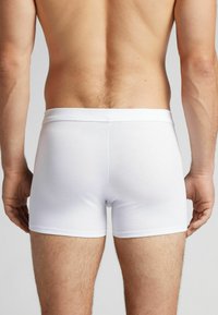 Vita bomullskalsonger med en mjuk midja, åtsittande design och slät textur, visas på en bar rygg.