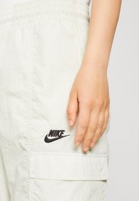 Ljust färgade cargobyxor gjorda av ett texturerat tyg, med ett elastiskt midjeband och en svart broderad Nike-logotyp på fickan.