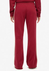 Maroon sweatpants with wide legs, elastic waistband, and cream side stripes. Soft fabric texture and relaxed fit, suitable for casual wear.