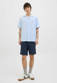Chemise à manches courtes bleu clair avec un fit décontracté, associée à un short navy, des chaussettes grises et des baskets blanches avec des touches de bleu.