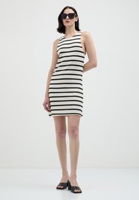 Ärmelloses gestreiftes Kleid in Creme und Schwarz, gerippte Textur, knielang, kombiniert mit schwarzen Mules und oversized Sonnenbrille.
