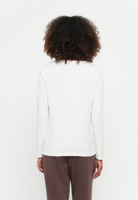 Witte geribde lange mouw top met een relaxte fit, voorzien van een ronde halslijn en een rechte zoom, gedragen met een paar bruine broeken.