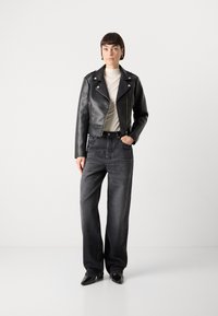 Zwarte leren cropped bikerjack met zilveren hardware, gecombineerd met hoge zwarte jeans en puntige zwarte schoenen. Effen crèmekleurige top.