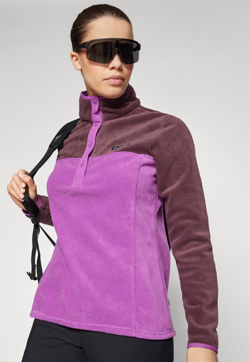 Fleece pullover in paars en bruin, met een hoge kraag, knopenlijst en een logo detail op de borst. Gladde textuur en ontspannen pasvorm.