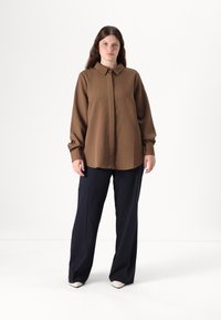 Brown striped long-sleeve shirt with a collar, paired with navy wide-leg trousers. The fabric appears smooth with a slight sheen.