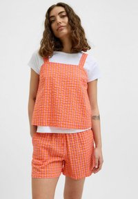 Hravý crop top s oranžovo-ružovým kockovaným vzorom so šnúrkami a zodpovedajúcimi šortkami, oboje vyrobené z ľahkej tkaniny. Má voľný strih a štvorcový výstrih.