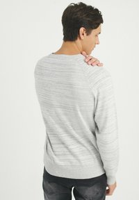 Suéter gris a rayas hecho de material suave, con un escote redondo y puños acanalados, combinado con jeans oscuros. Se muestra vista trasera.
