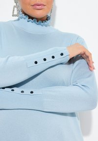 Helles blaues Sweatshirt mit einem rüschigen hohen Kragen und langen Ärmeln, verziert mit schwarzen Knopf-Details an den Bündchen. Weicher Strickstoff.